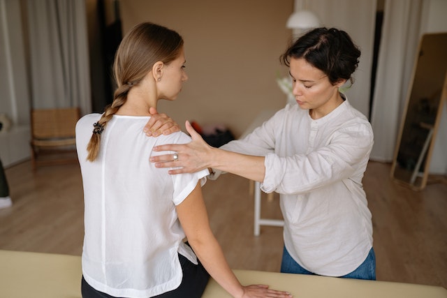 A massage therapist massaging a woman’s shoulder. 