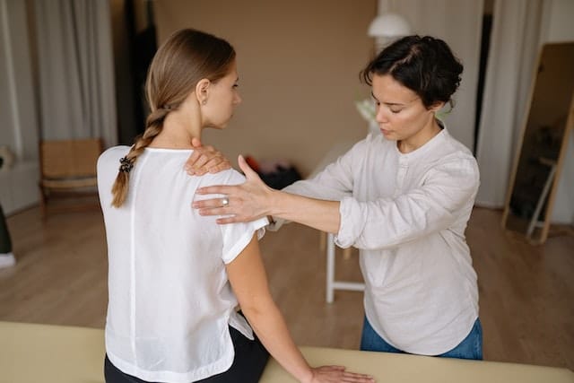 A massage therapist massaging a woman’s shoulder.